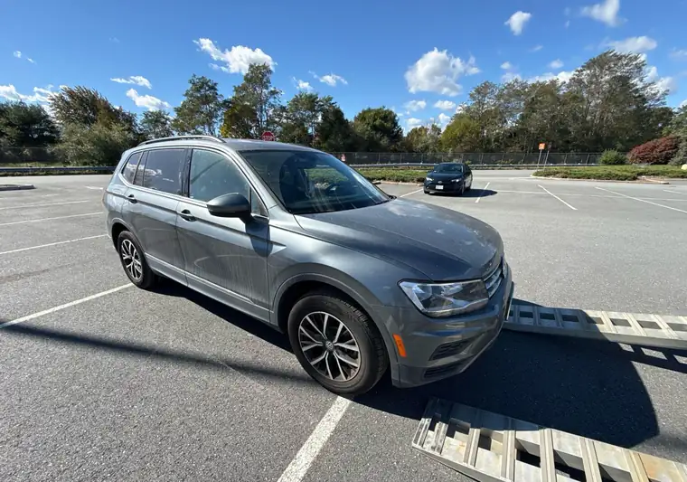 The same Volkswagen Tiguan in a parking lot at delivery in Massachusetts, next to car-carrier ramps