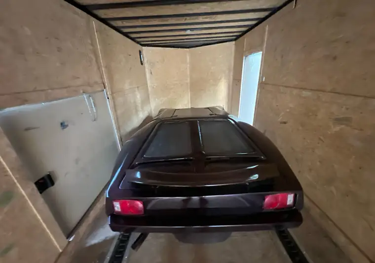 A dark maroon 1982 Cimbria SS strapped down inside a plywood-lined enclosed car trailer at pickup in Des Moines, Iowa