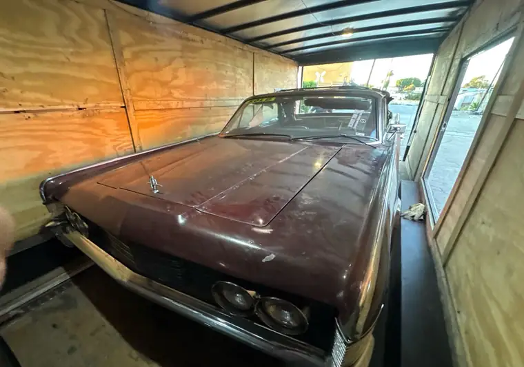 Maroon 1965 Lincoln Continental convertible inside a plywood-lined enclosed trailer at pickup in Los Angeles, California