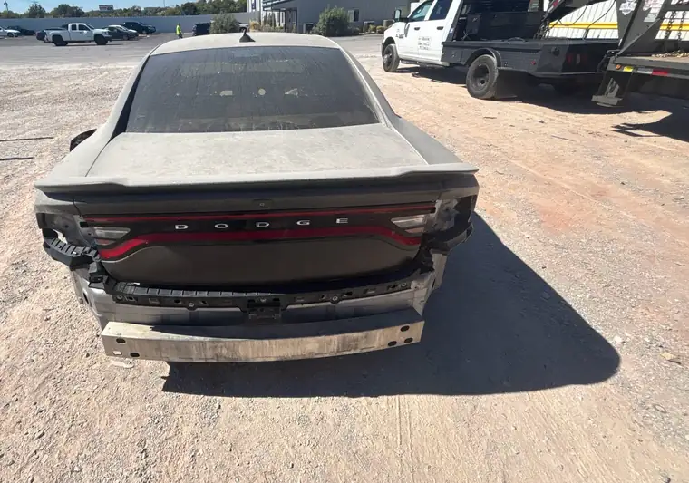 Gray 2015 Dodge Charger, rear view, with a damaged rear bumper in a gravel salvage yard in Oklahoma City, Oklahoma