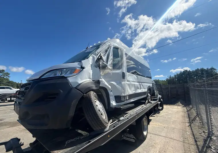 White 2023 Ram ProMaster van with front and side damage on a flatbed tow truck in Shirley, Massachusetts
