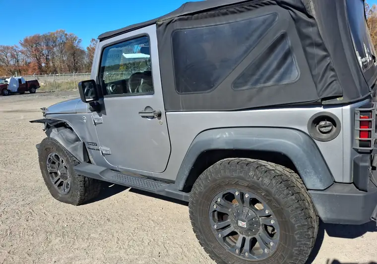 Silver 2013 Jeep Wrangler with front-end damage on a gravel lot in Elkton, Maryland