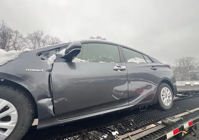 Gray 2020 Toyota Prius Prime with front-end damage on an open car carrier in snow at pickup in White Plains, Maryland