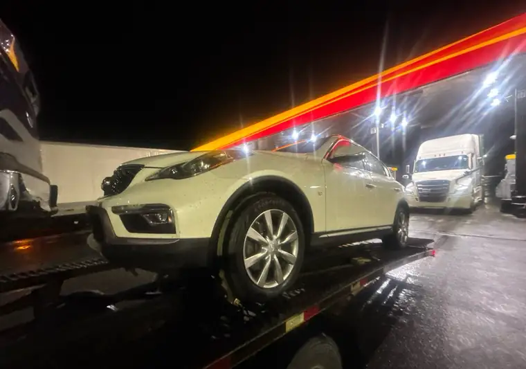 White 2016 Infiniti QX50 loaded on an open car carrier at night in Canaan, New York