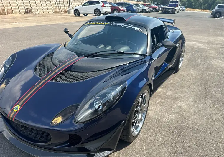 Dark blue 2007 Lotus Exige with a gold and red stripe in a parking lot in Boulder, Colorado