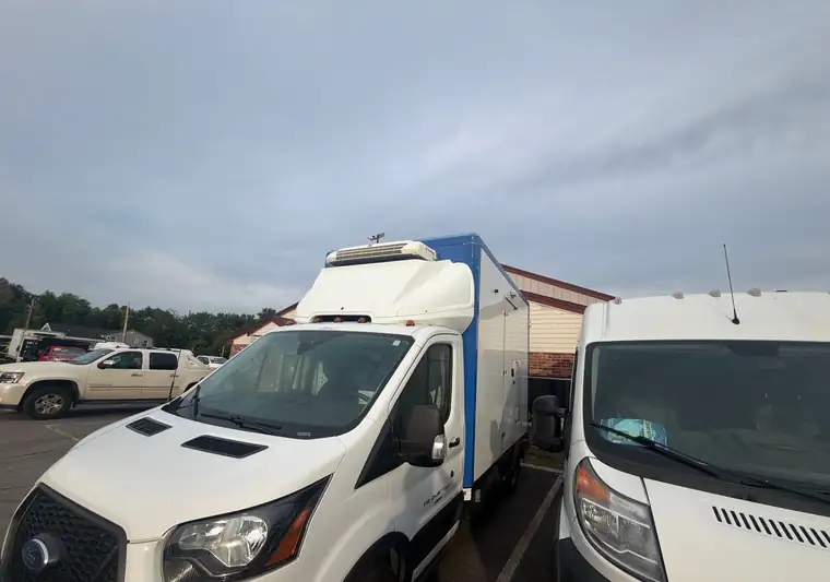 The same Ford Transit box truck beside a Ram van at a dealer lot in Rowley, Massachusetts