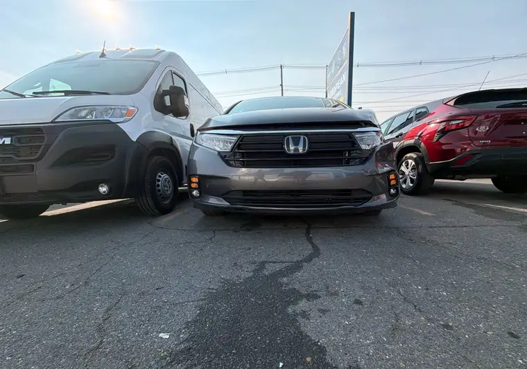 The same Honda Odyssey with front damage beside a Ram van at delivery in Brockton, Massachusetts