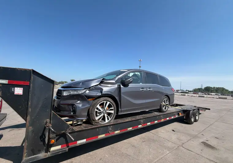 Gray 2024 Honda Odyssey with front-end damage on a gooseneck trailer at a Copart yard in Woodhaven, Michigan