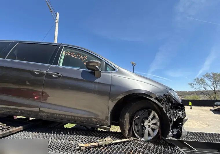 Gray 2020 Chrysler Voyager with front-end damage loaded on a car hauler at the IAA yard in Saint Paul, Minnesota