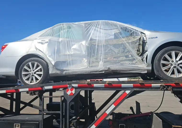 Silver Toyota Camry Hybrid with collision damage wrapped in plastic on a car hauler in Springfield, Missouri