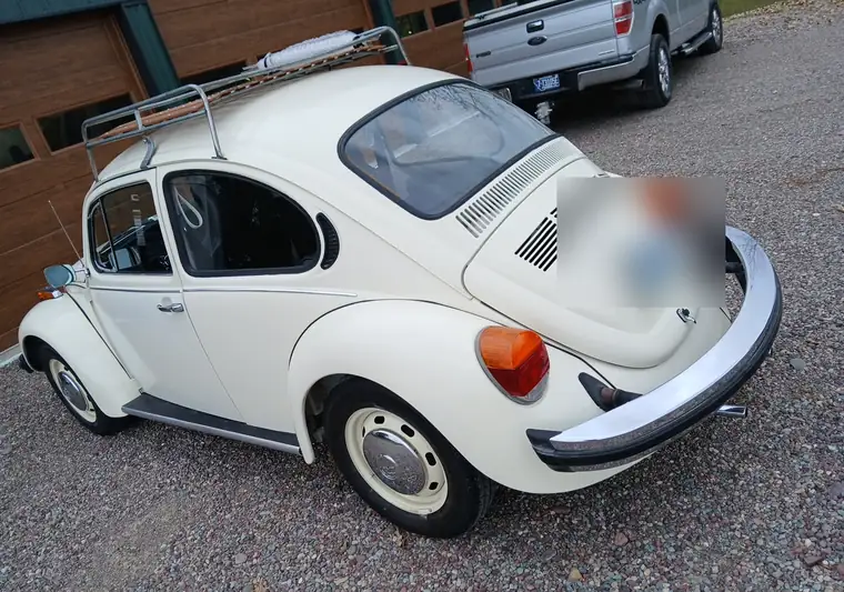 Cream 1974 Volkswagen Beetle with a roof rack on a gravel driveway at pickup in Kalispell, Montana
