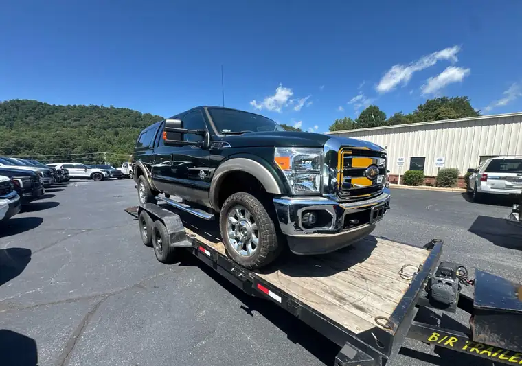 Dark green and tan 2012 Ford F-250 Super Duty with a bed cap on a tilt trailer at pickup in Sylva, North Carolina