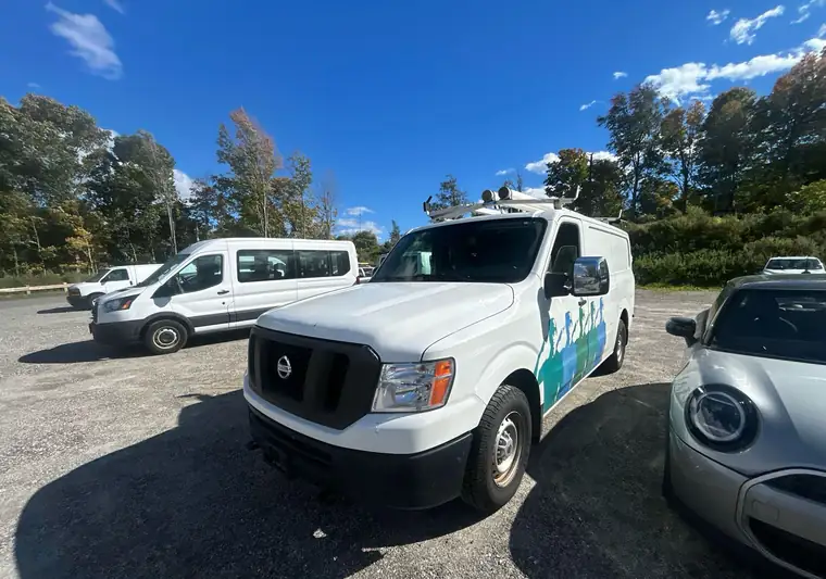 White 2019 Nissan NV cargo van with a roof rack and a colorful side graphic at pickup in Brewster, New York