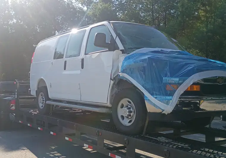 White 2025 Chevrolet Express van with a blue tarp over the damaged front end on a car hauler at pickup in Exeter, Rhode Island