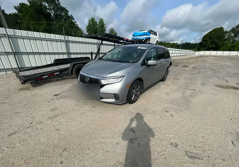 Silver 2021 Honda Odyssey minivan with rear damage at a car-hauler lot at pickup in Harleyville, South Carolina (dealer tag blurred)