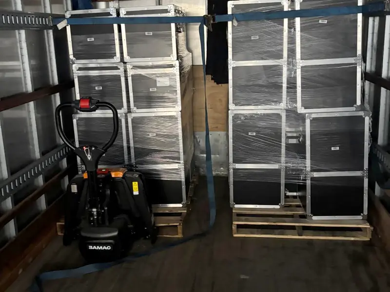 Stacked road cases on pallets strapped in a box truck next to an electric pallet jack